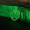 Lifestyle photo of single smooth-back Slay the Spire Snake Ring in glow-in-the-dark translucent green on wood block glowing in darkness