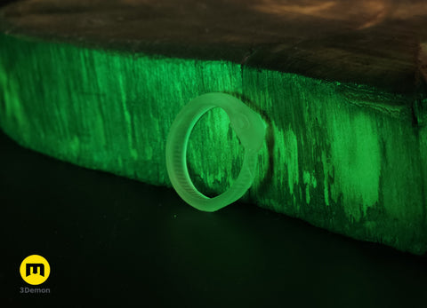 Lifestyle photo of single smooth-back Slay the Spire Snake Ring in glow-in-the-dark translucent green on wood block glowing in darkness