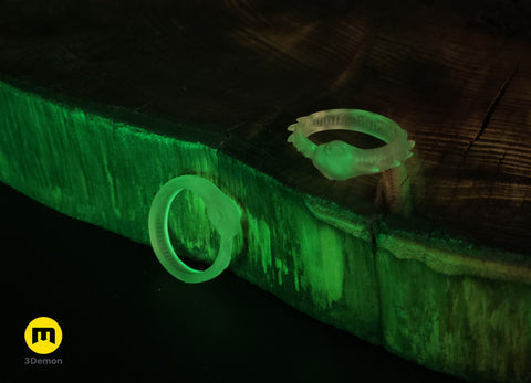 Lifestyle photo of two translucent glow-in-the-dark Slay the Spire Snake Rings on dark wood block emitting vivid green glow in low light