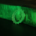 Lifestyle photo of single spiked-variant Slay the Spire Snake Ring in glow-in-the-dark translucent green on wood glowing brightly in dark