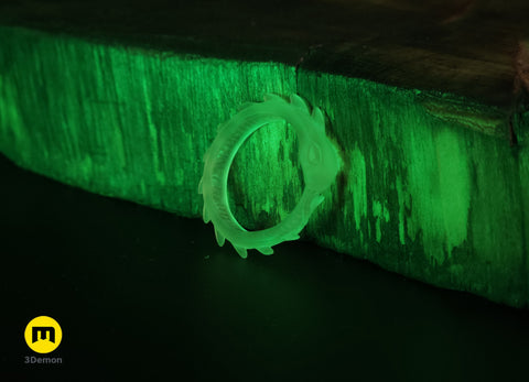 Lifestyle photo of single spiked-variant Slay the Spire Snake Ring in glow-in-the-dark translucent green on wood glowing brightly in dark