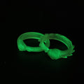 Lifestyle photo of two translucent glow-in-the-dark Slay the Spire Snake Rings together on dark surface showing both smooth and spiked variants