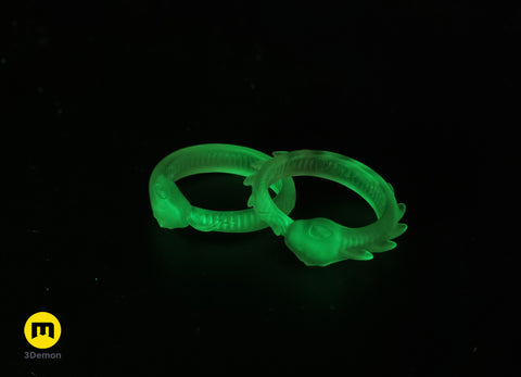 Lifestyle photo of two translucent glow-in-the-dark Slay the Spire Snake Rings together on dark surface showing both smooth and spiked variants