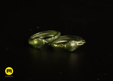 Lifestyle photo of two 3D printed Slay the Spire Snake Rings metallic green alternate angle on black surface showing head and tail detail