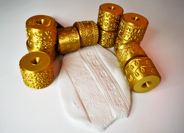 All 11 Christmas texture rollers in metallic gold PLA arranged around white clay slab showing impressed holly snowflake and star patterns from the complete middle roller set