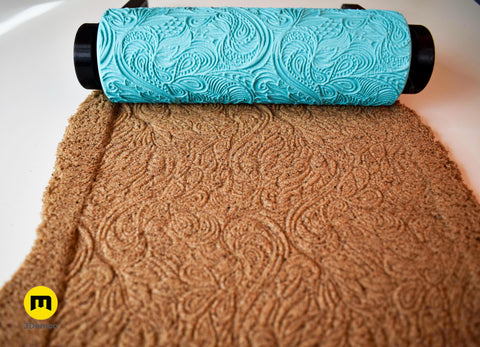 Photo of single turquoise 3D printed mandala roller next to its perfect imprint in brown sand showing crisp centered large mandala circle pattern