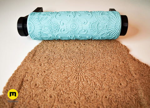 Photo of turquoise 3D printed starburst sunburst mandala pattern roller lying next to its clear geometric concentric star shape imprint in brown clay