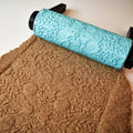 Top-down photo of multiple turquoise mandala texture rollers and their corresponding distinct mandala imprints in brown clay slab showing set variety