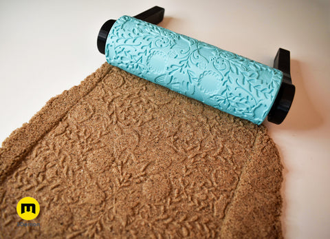 Top-down photo of multiple turquoise mandala texture rollers and their corresponding distinct mandala imprints in brown clay slab showing set variety