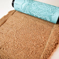Close-up photo of turquoise 3D printed multi-layered complex mandala roller with deep precise imprint in brown sand showing high detail output