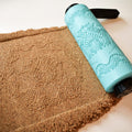 Photo of turquoise 3D printed complex geometric concentric circles and triangles mandala roller alongside deep precision imprint in brown clay