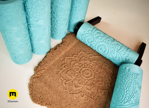 Close-up product photo of multiple turquoise 3D printed mandala texture rollers standing vertically showing fine geometric and floral embossed surface patterns