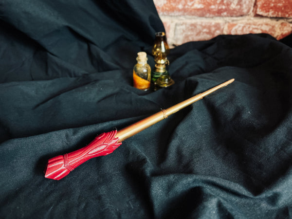 3D printed Wonder Woman magic wand cosplay prop with a red textured handle and golden shaft on black fabric.
