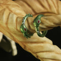 Cover lifestyle photo of two 3D printed Slay the Spire Silent Snake Rings metallic green finish with red eyes on beige finger display prop