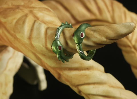 Cover lifestyle photo of two 3D printed Slay the Spire Silent Snake Rings metallic green finish with red eyes on beige finger display prop