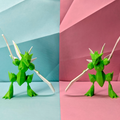 Two green scyther figurines on a split background of blue and pink. The right one has a larger abdomen.