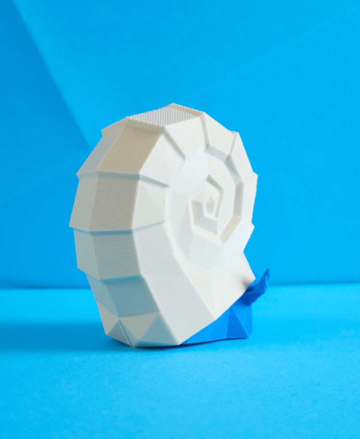 3D printed Omanyte STL collectible figure, white spiral shell, side view, plain blue background