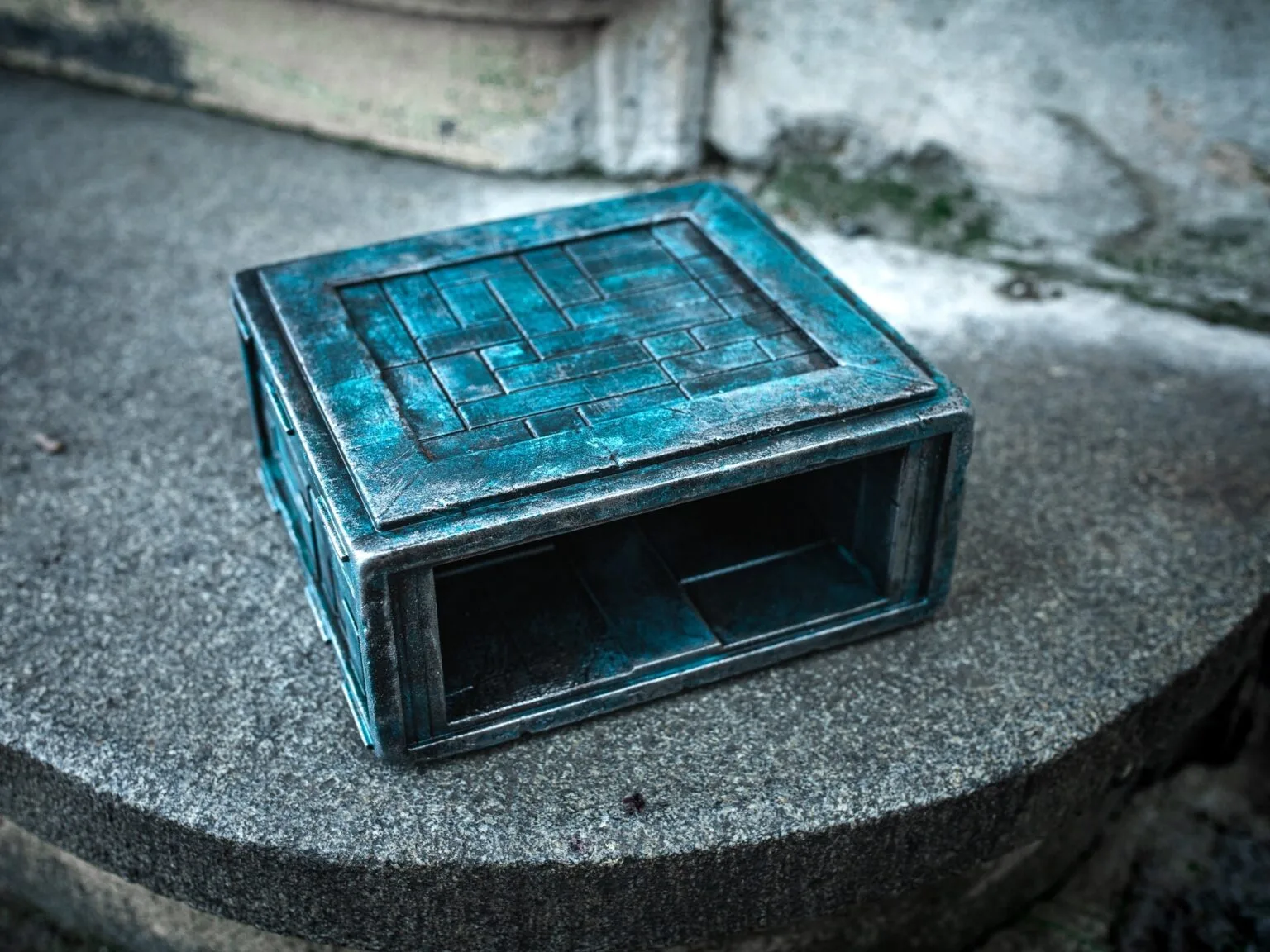 Lifestyle photo of Box of Pain STL, weathered blue metal 3D printed holder on stone steps