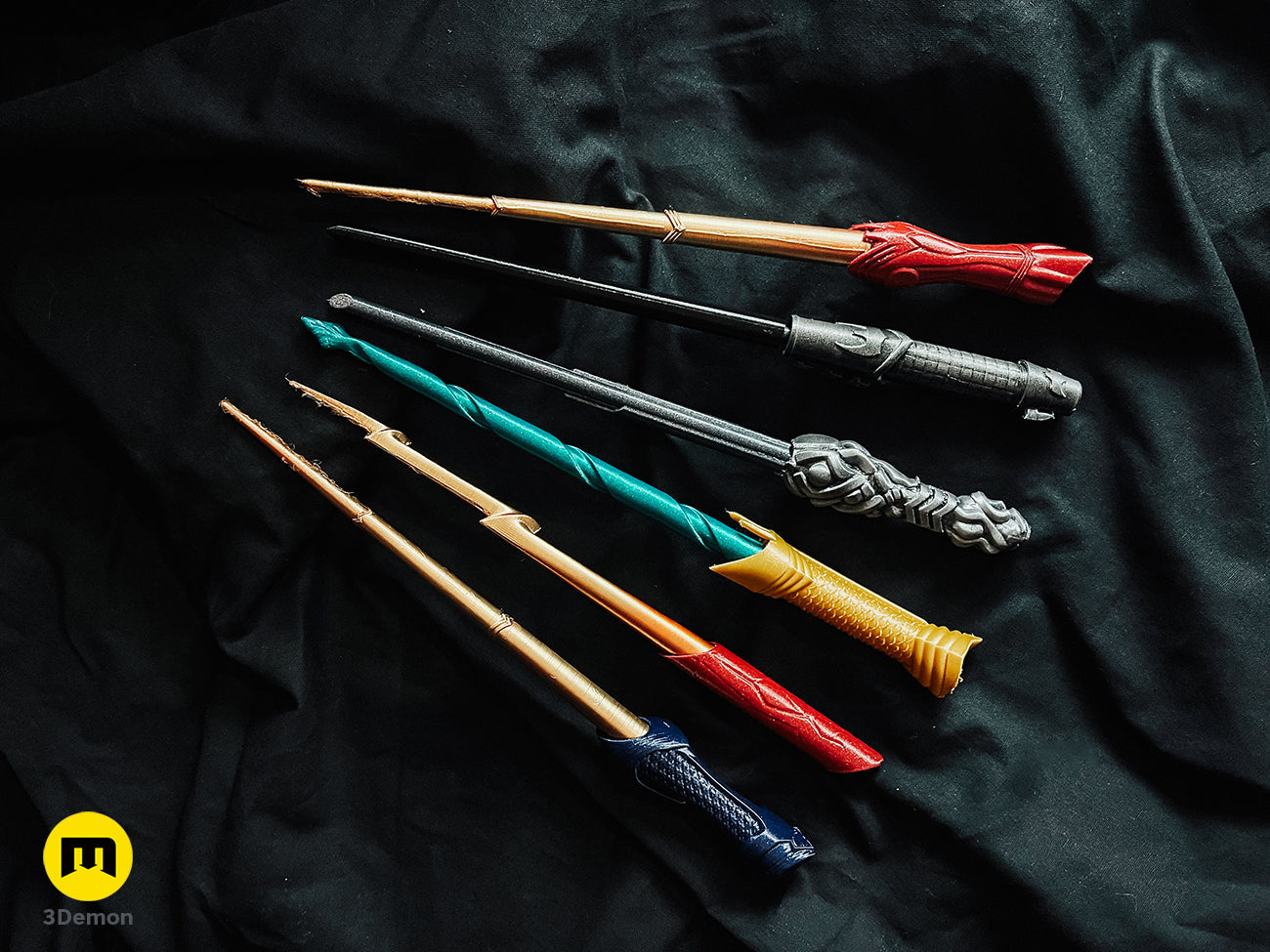 Collection of 3D printed magic wands featuring the red and gold Flash-themed wand cosplay prop on black fabric.