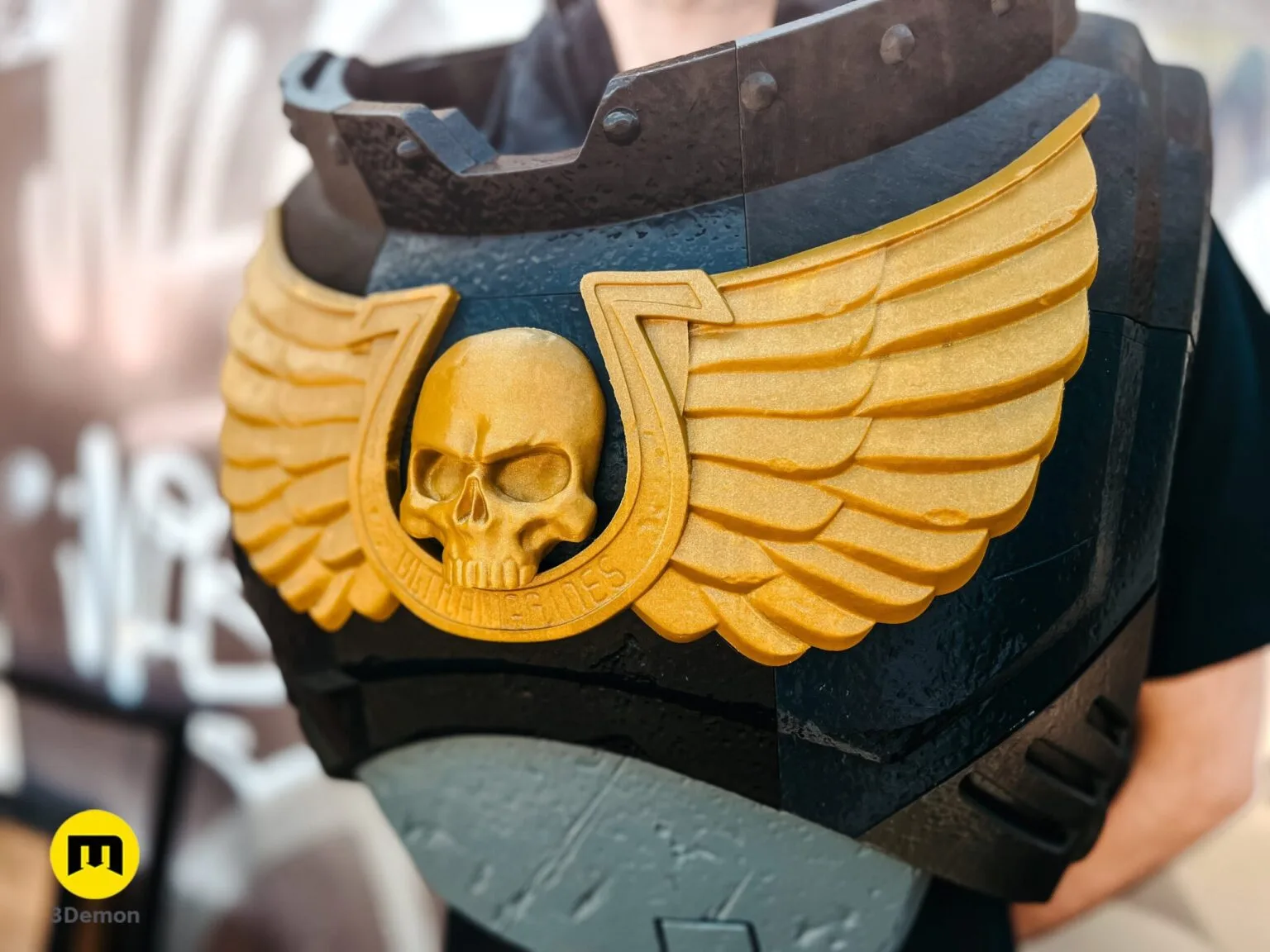 Close-up of a person wearing a black 3D printed Space Marine chest plate with a golden Aquila emblem.