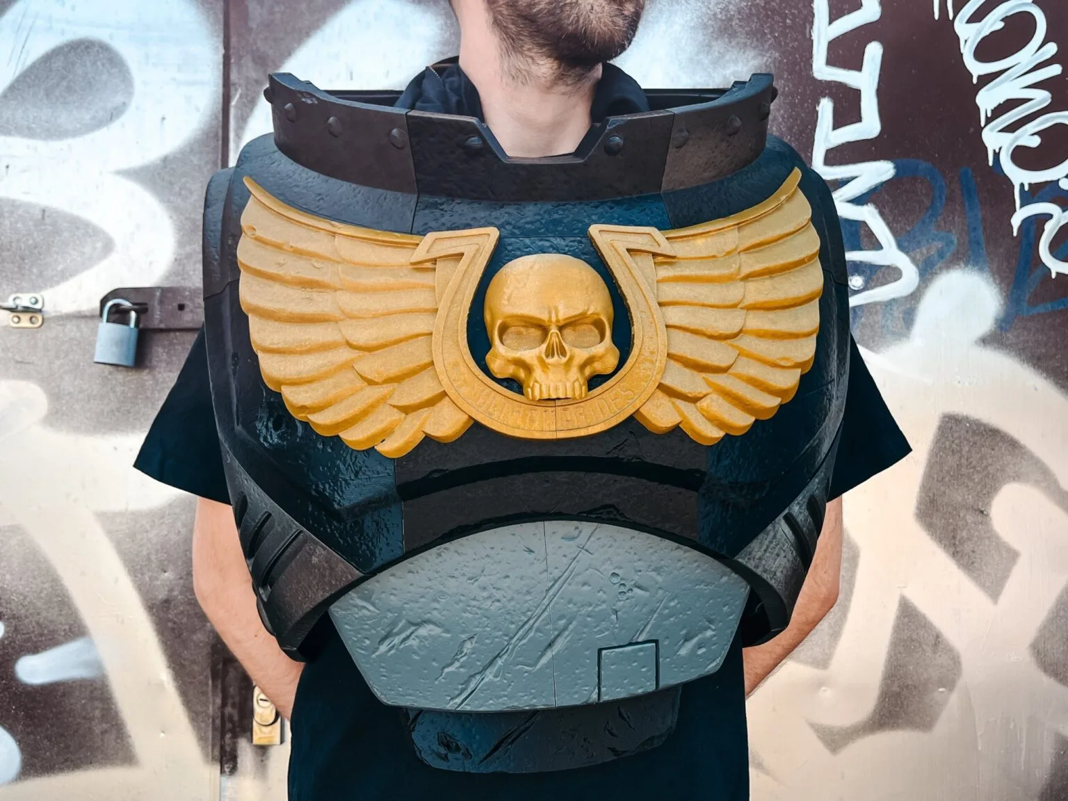 A person wearing a black 3D printed Space Marine chest plate with a large golden winged skull emblem.
