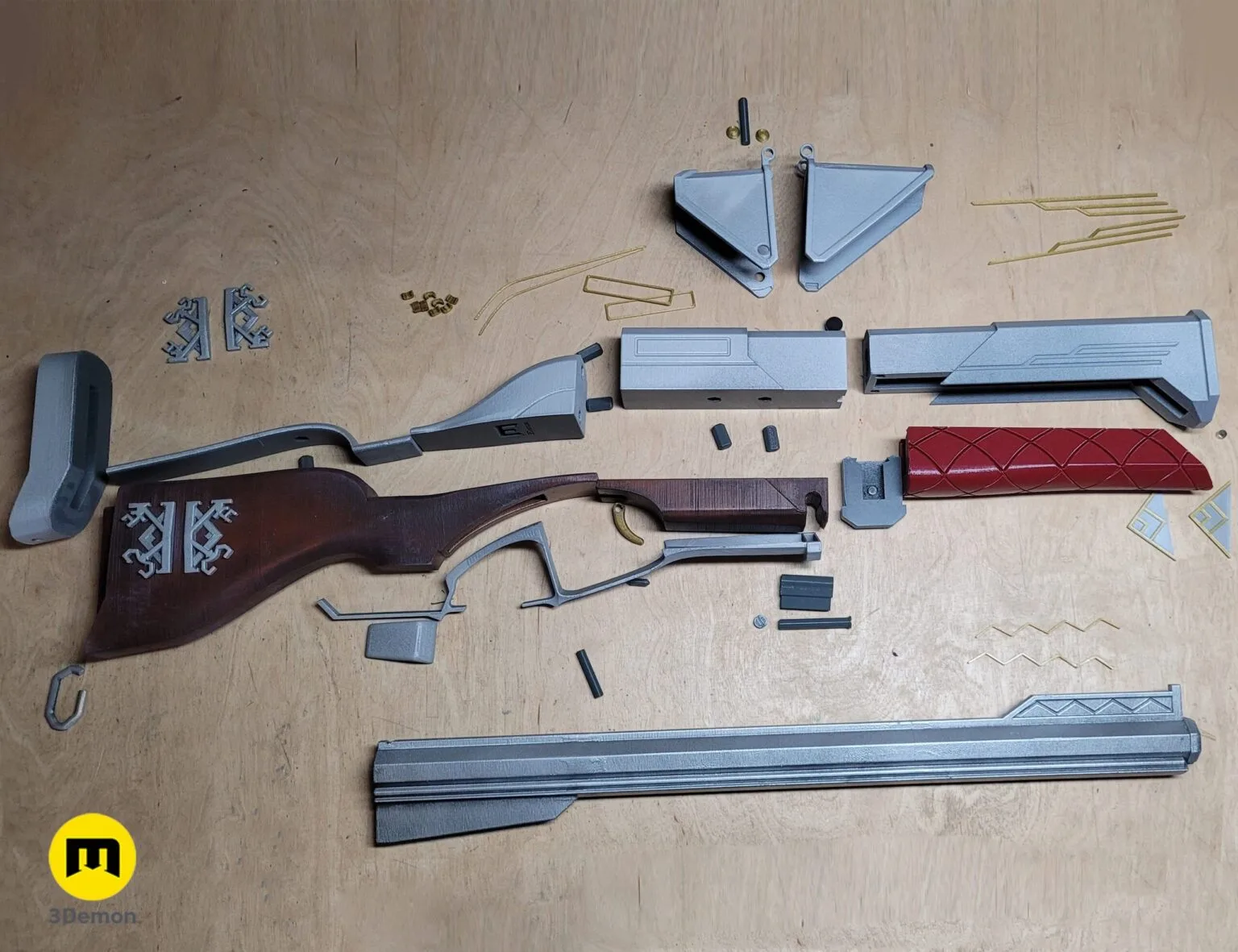 Disassembled parts of the 3D printed Caitlyn rifle replica, including the barrel, stock, and red grip.
