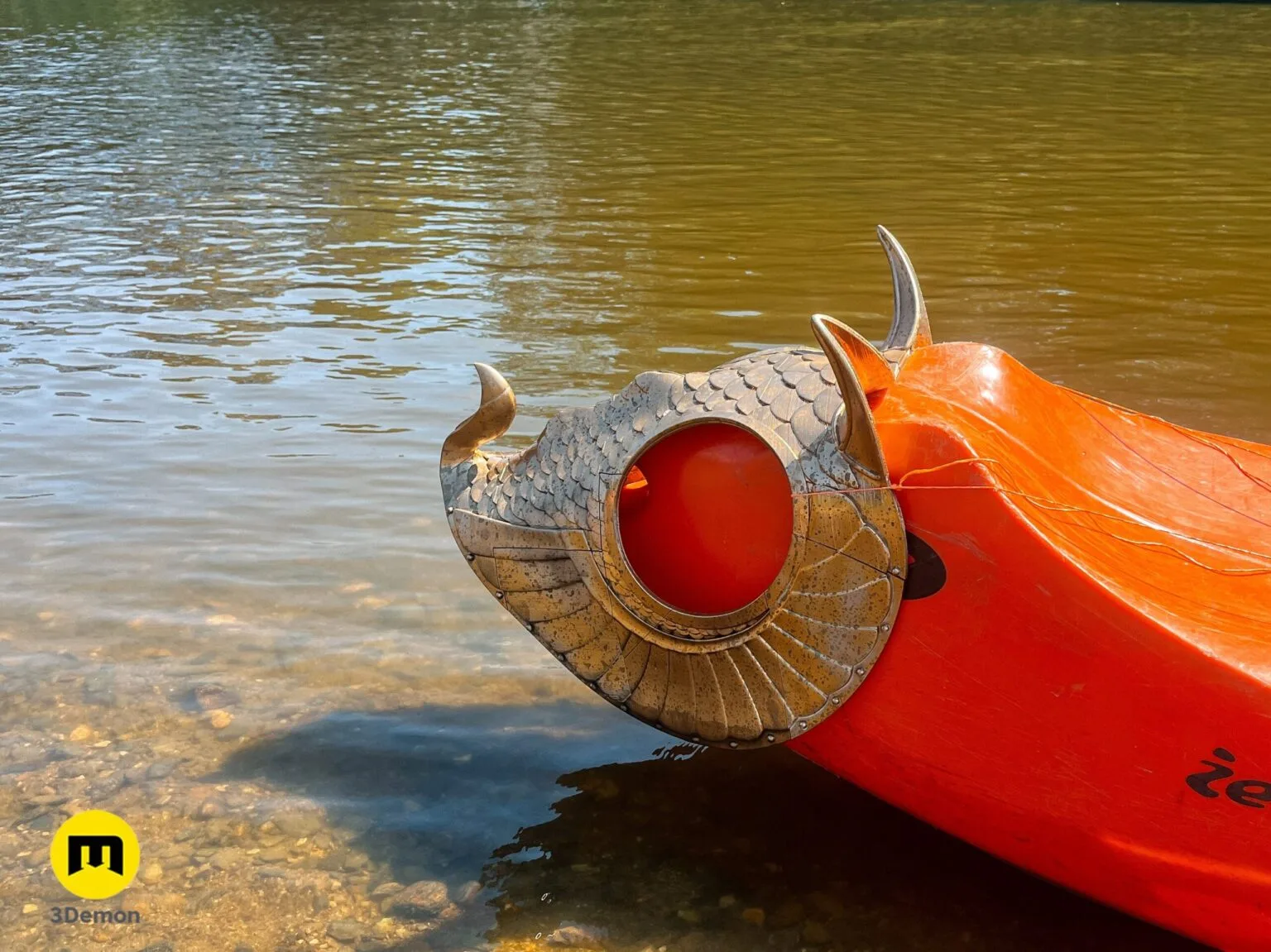 Close-up of golden 3D printed dragon horse armor mounted on the bow of an orange kayak.
