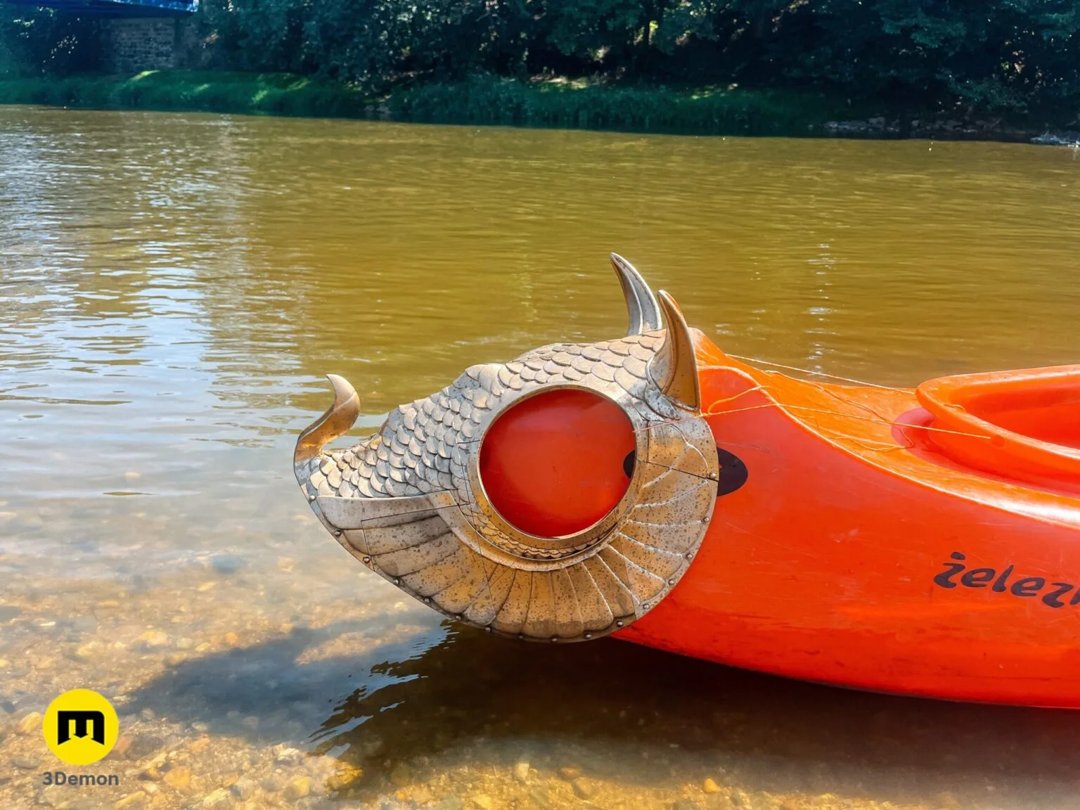 Golden 3D printed scaled armor piece on an orange kayak, outdoor natural lighting.