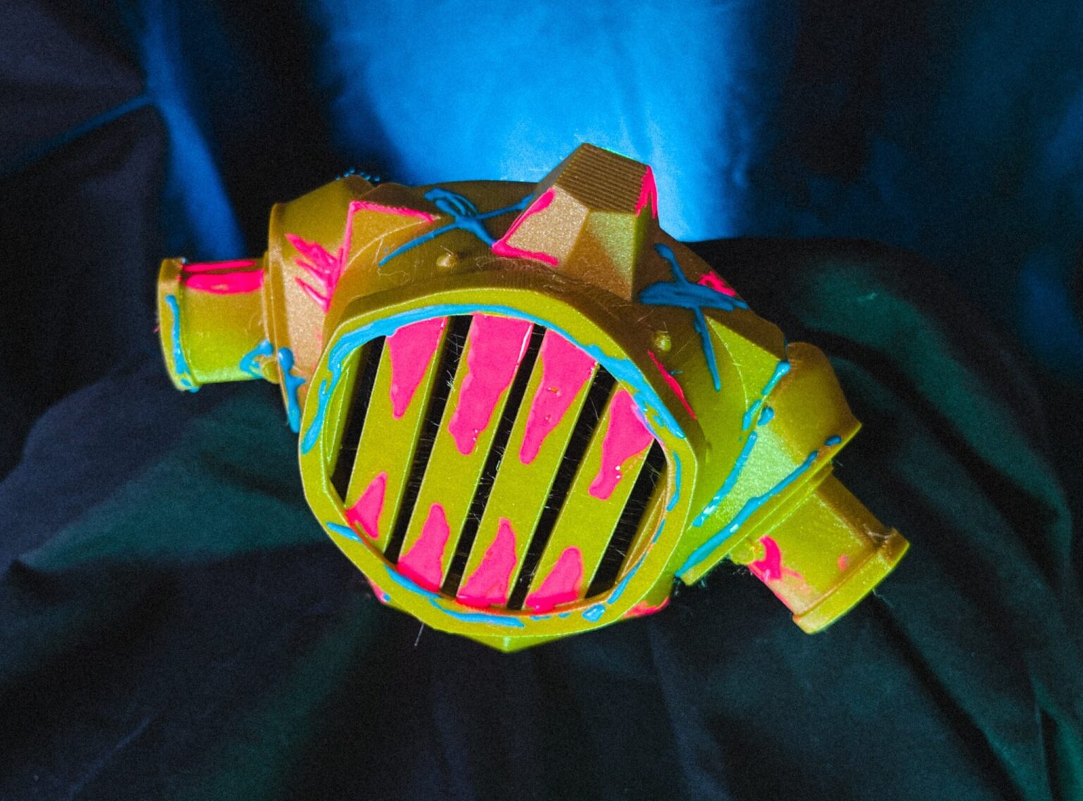 Painted 3D printed Jinx gas mask cosplay prop from Arcane, held in hand with gold and grey details.