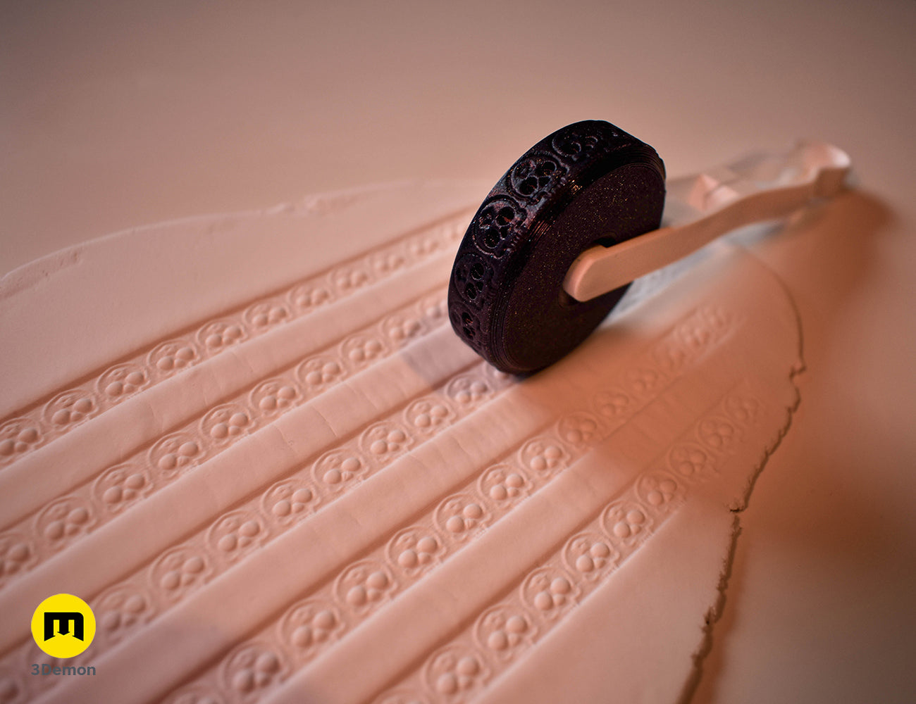 Black 3D printed stamp wheel with a white handle creating rows of crescent moon patterns on white clay.