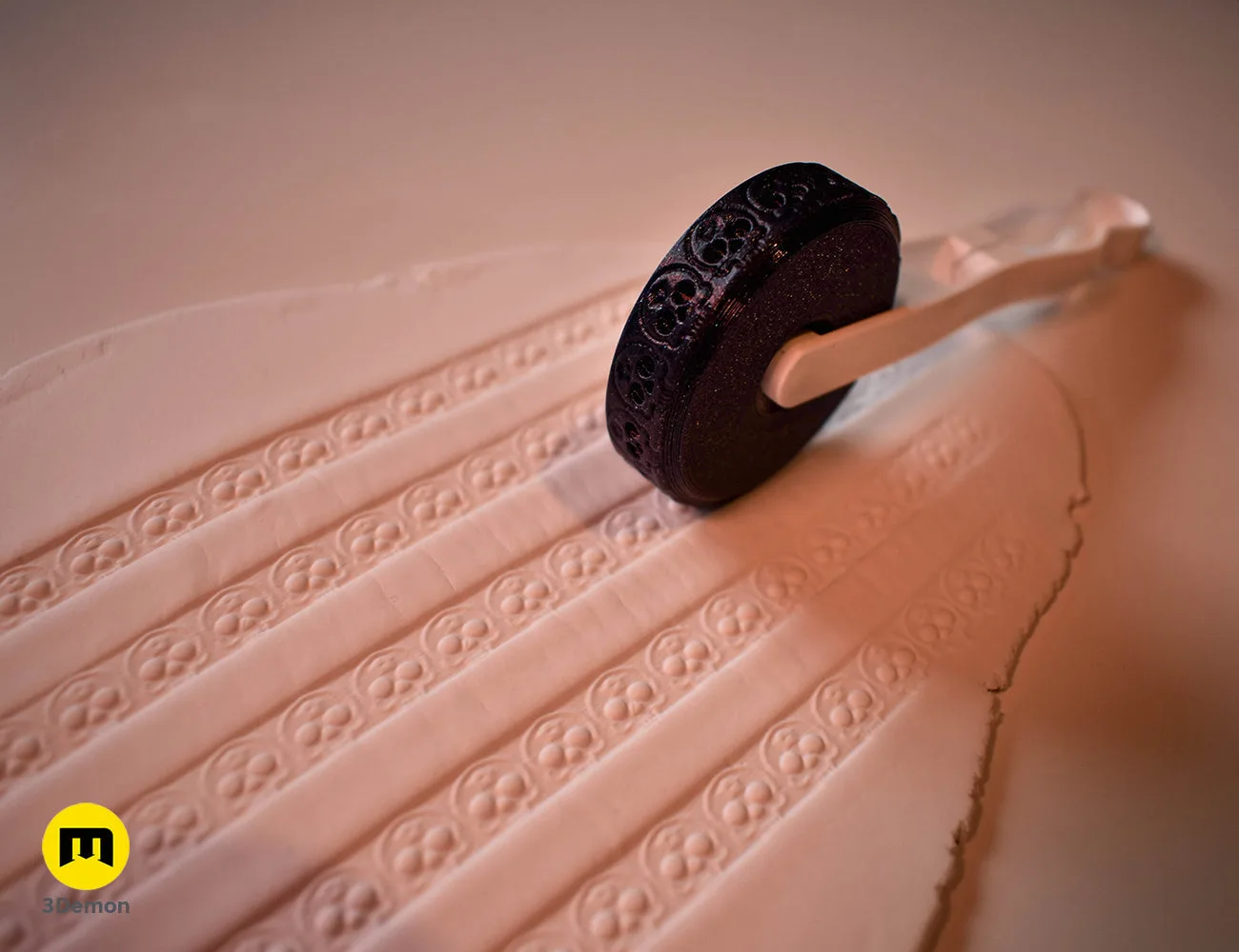 Black 3D printed stamp wheel with a white handle creating rows of crescent moon patterns on white clay.