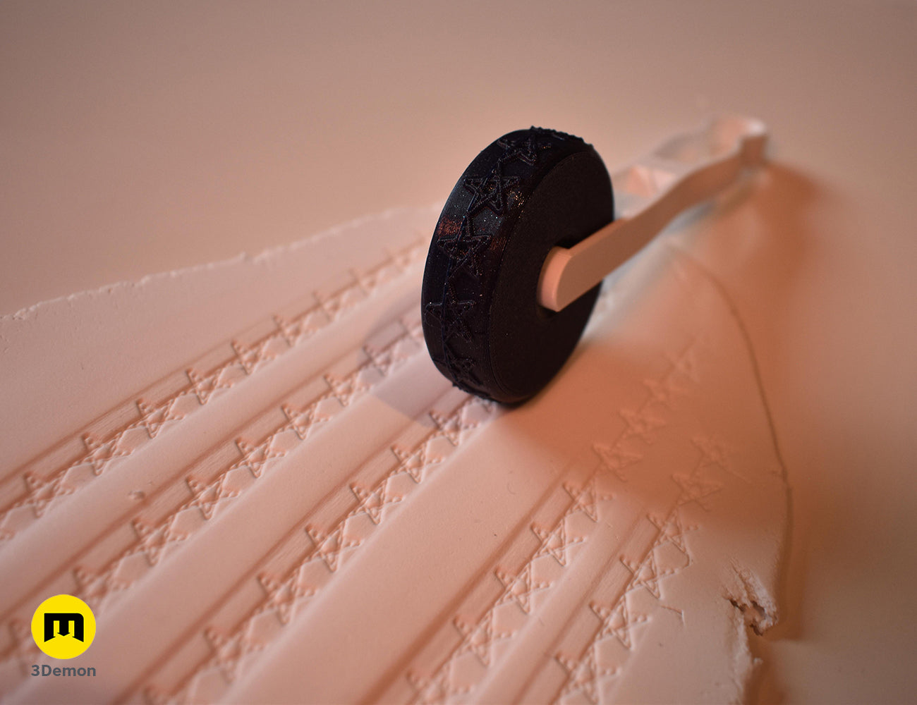 Black 3D printed stamp wheel with a white handle creating rows of star patterns on white clay.