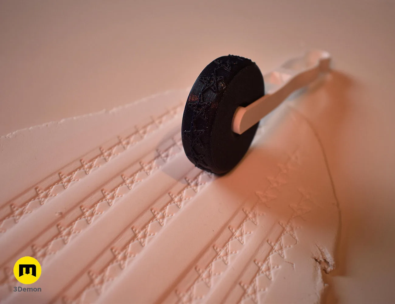 Black 3D printed stamp wheel with a white handle creating rows of star patterns on white clay.