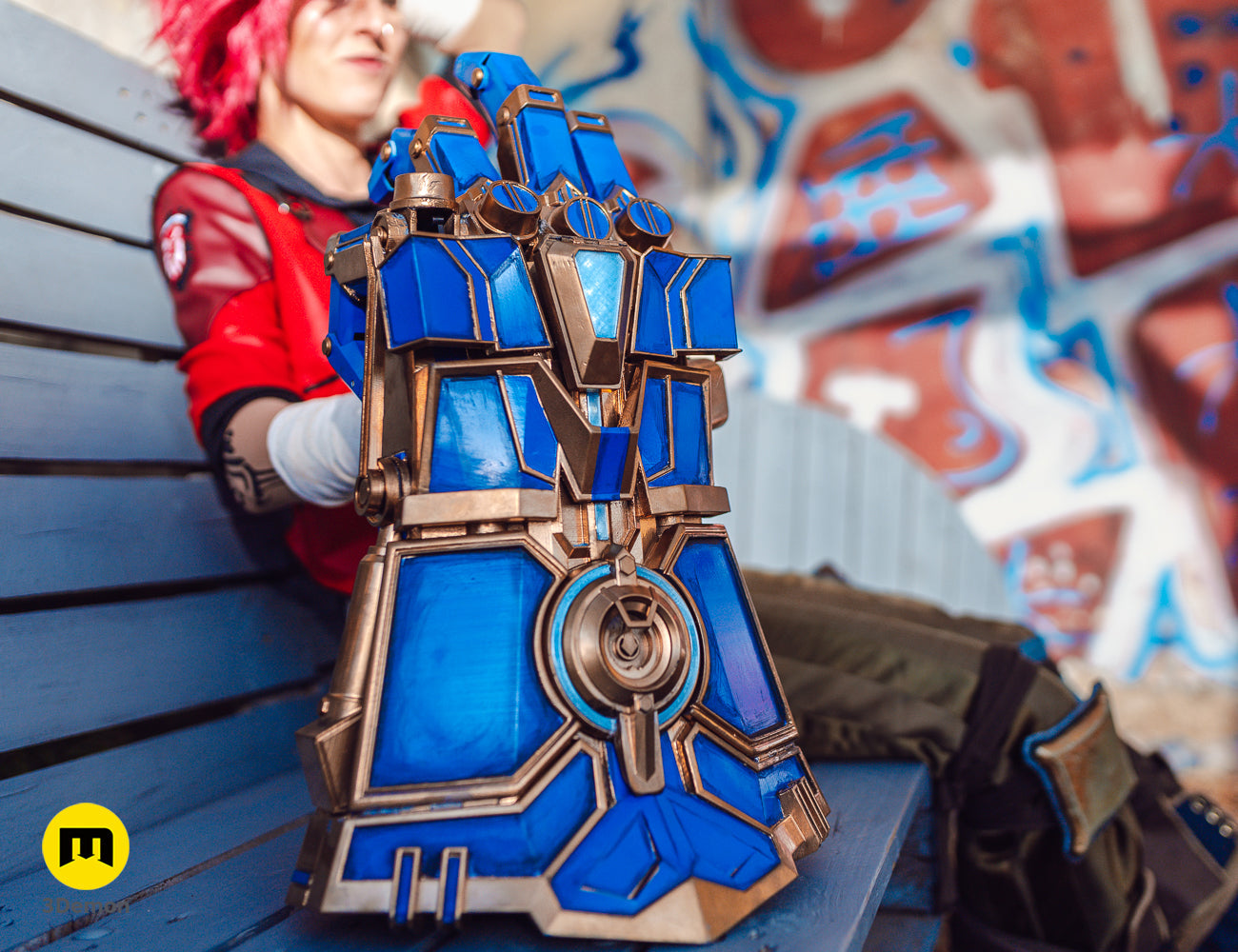 Close-up of a 3D printed blue and gold Arcane Vi mechanical gauntlet prop resting on a wooden bench.