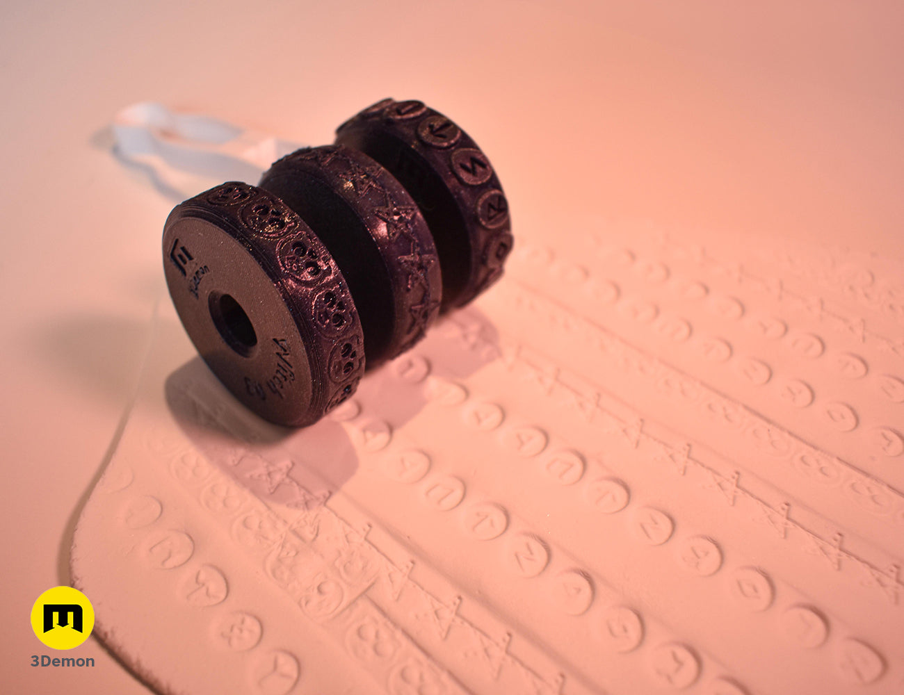 Close-up of a purple 3D printed stamp wheel creating a row of various occult symbols on white clay.