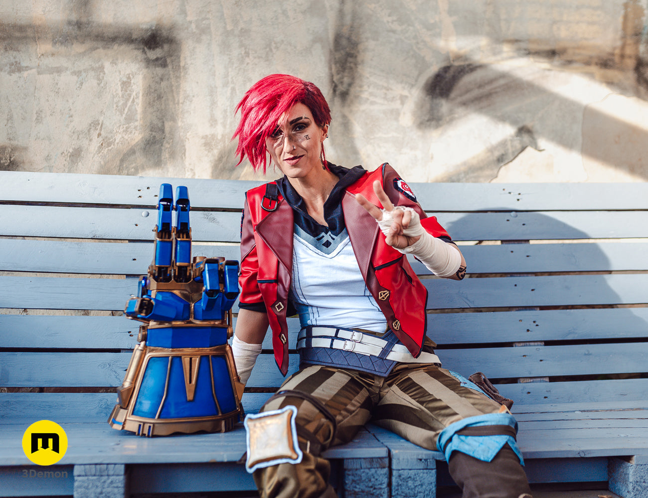 Vi cosplayer sitting on a blue bench with a 3D printed mechanical gauntlet prop from Arcane.