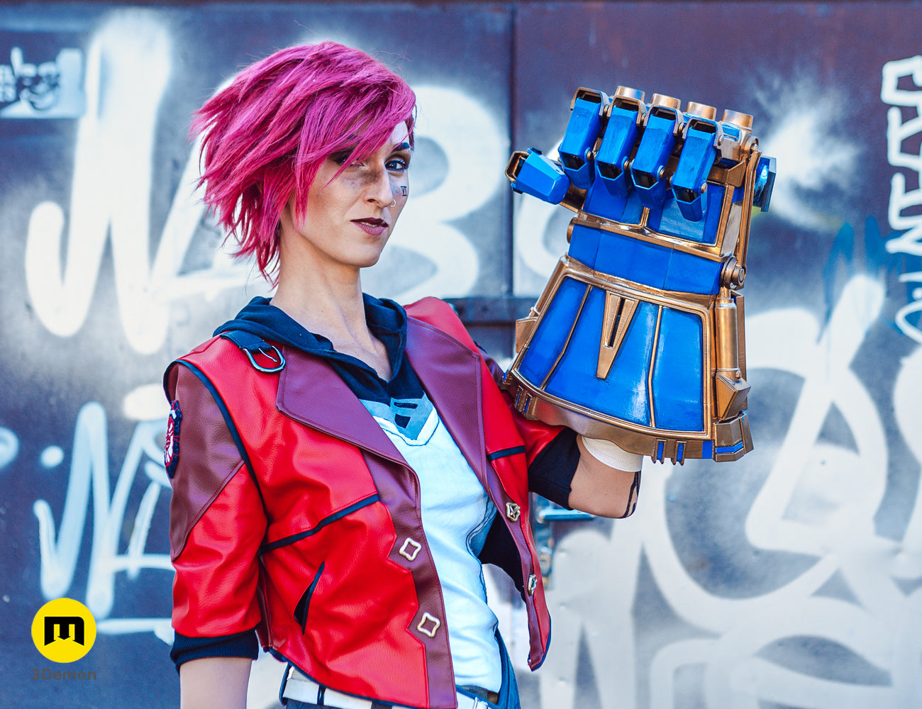 Vi cosplayer with pink hair in a red leather jacket posing with the 3D printed mechanical gauntlet.
