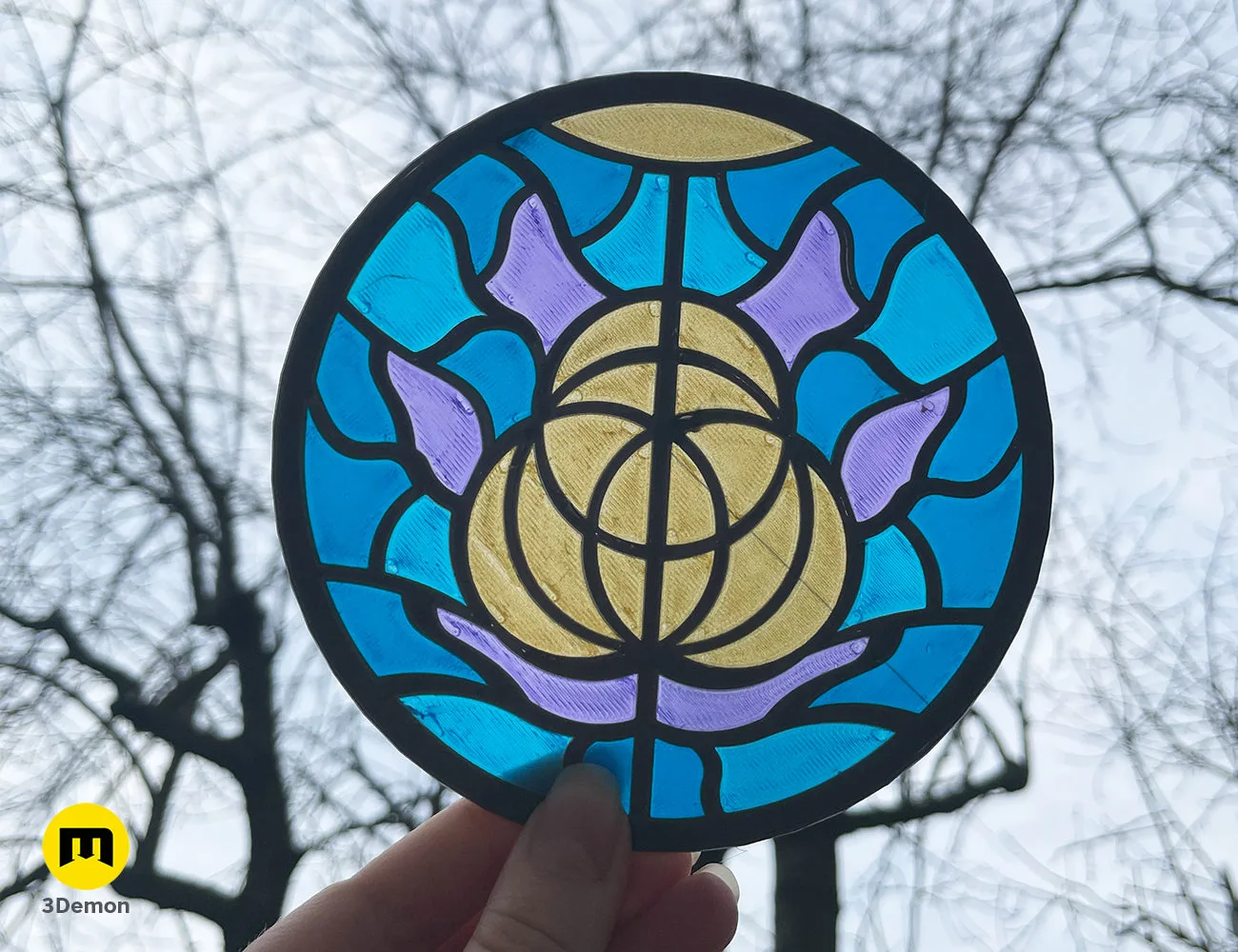 Circular 3D printed Elden Ring stained glass logo with water droplets, held against a cloudy sky – Elden Ring Stained Glass 3D print | 3Demon