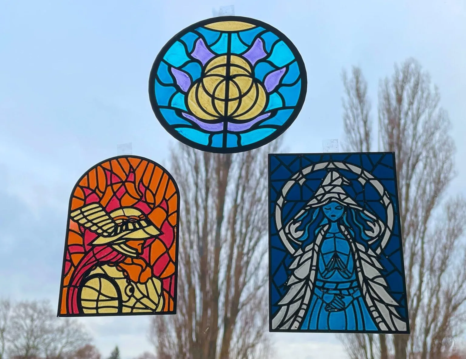 Three 3D printed Elden Ring stained glass panels (Elden Ring logo, Malenia, Ranni) on a window – Elden Ring Stained Glass 3D print | 3Demon