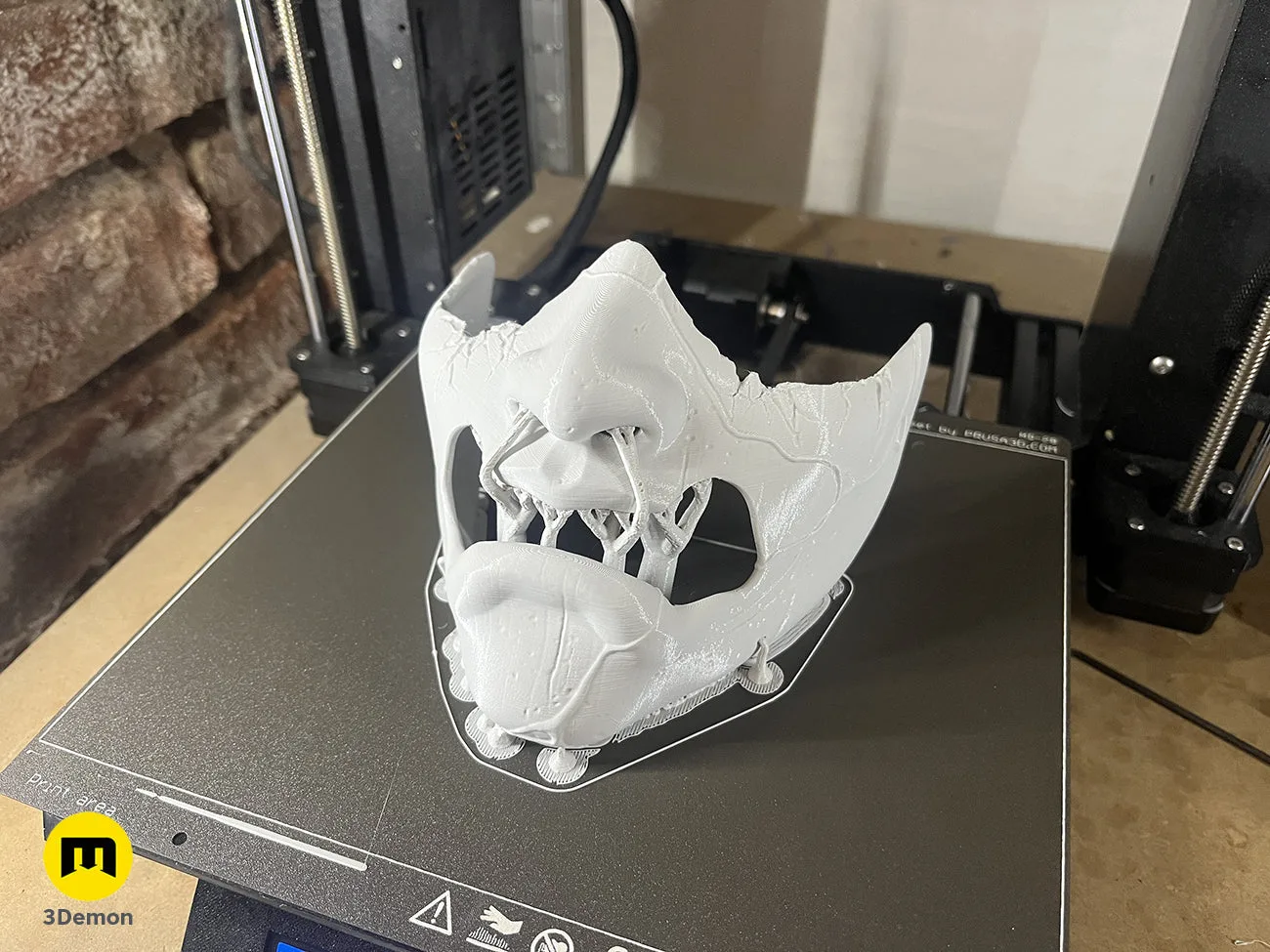 Unpainted white 3D printed samurai mask with gold teeth on printer bed, showing raw print quality – Ghost of Yotei Samurai Mask 3D print | 3Demon
