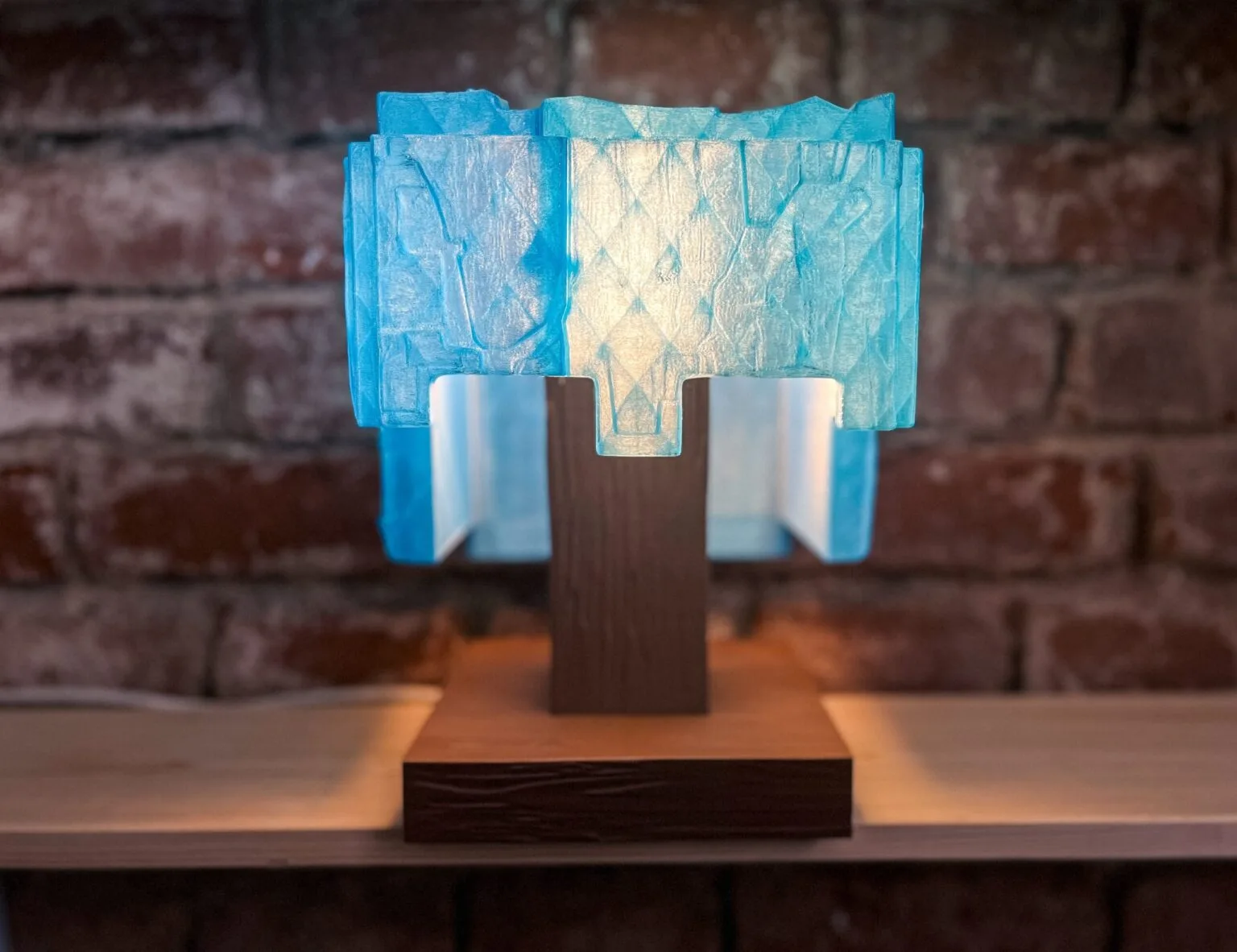 Lifestyle photo of 3D printed Minecraft diamond helmet lamp glowing vivid blue light on blocky wooden-texture stand in dark room showing translucent blue pixel helmet illuminated from within