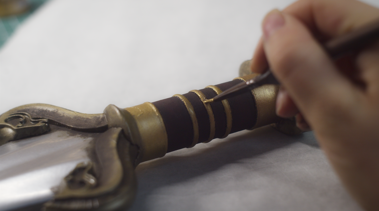 Holding the sword by its gold crossguard and banded grip