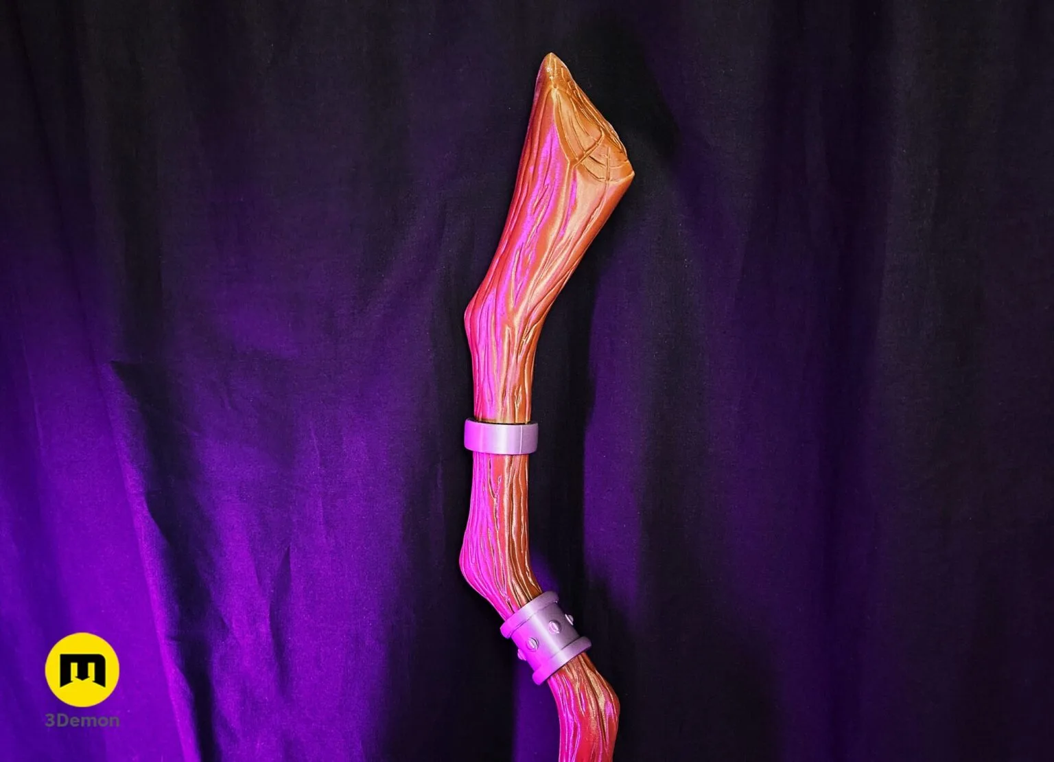 Lifestyle photo of finished 3D printed Fern Staff Frieren lying horizontal on black cloth showing full tan light-brown wood-grain painted shaft with silver metallic accent bands