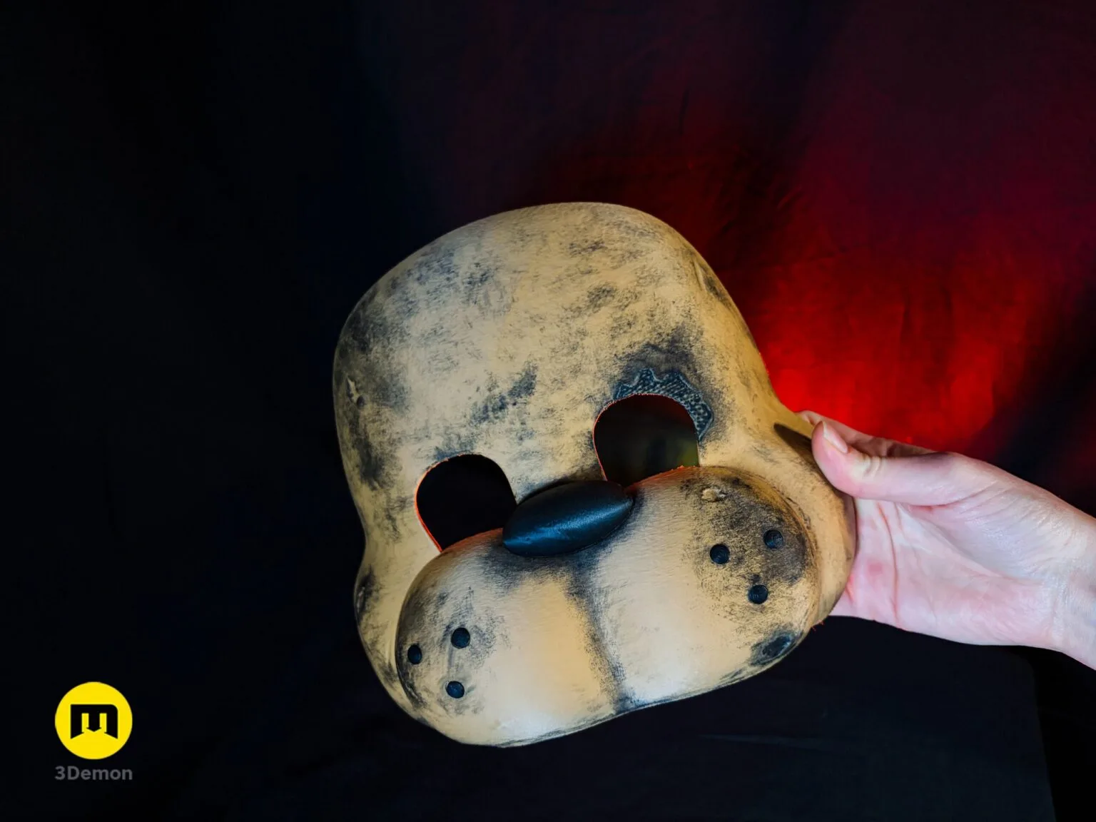 Lifestyle photo of person in black hoodie wearing finished Freddy Fazbear movie mask looking directly at camera showing glowing red eyes brown fur weathered texture